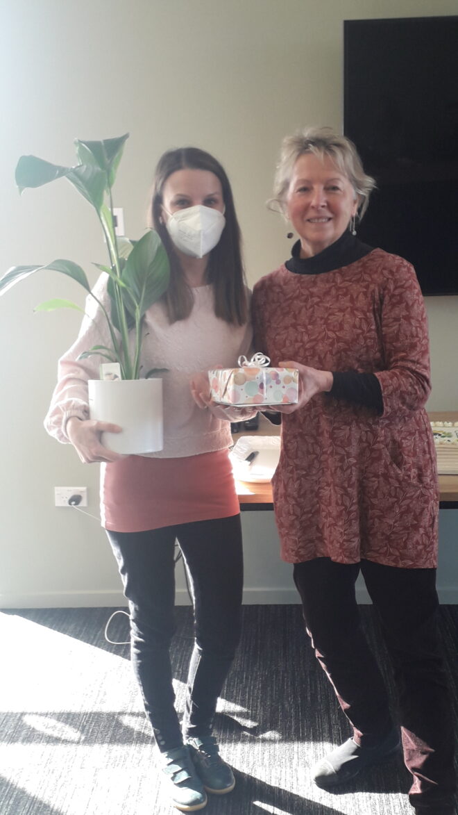 Two woman holding a potted plant and a small wrapped gift